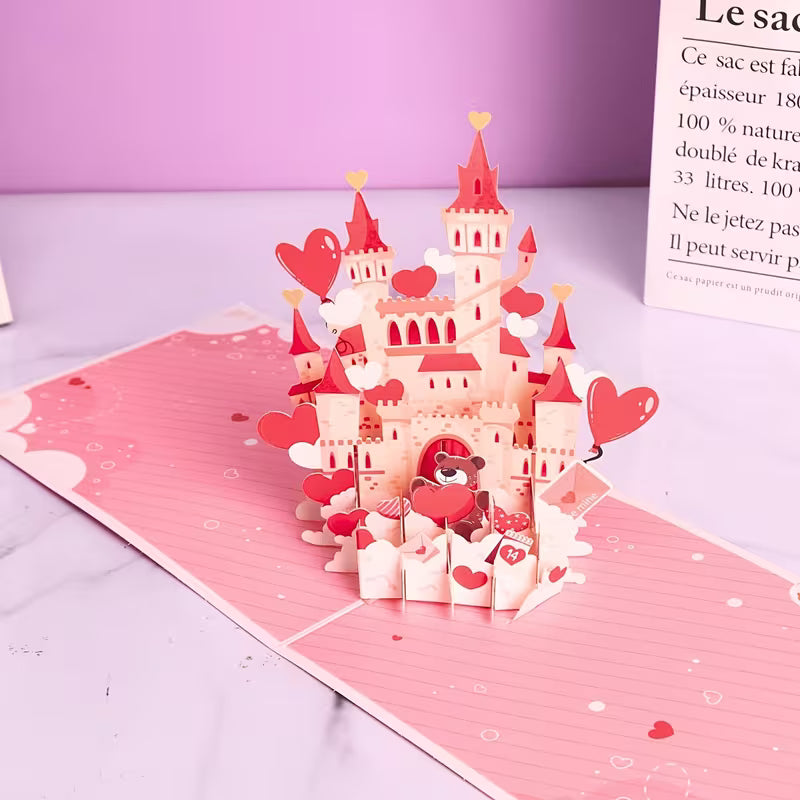 Avattu 3D pop-up -kortti, josta nousee näyttävä vaaleanpunainen linna täynnä sydämiä ja suloinen nallekarhu, kuvattuna vaaleanpunaisella alustalla.