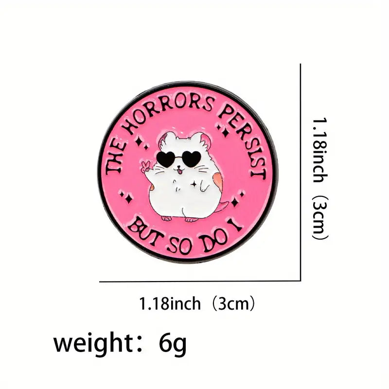 Pyöreä vaaleanpunainen emalinasta, jossa aurinkolaseja käyttävä valkoinen hamsteri tekee rauhanmerkin. Teksti: The Horrors Persist But So Do I.