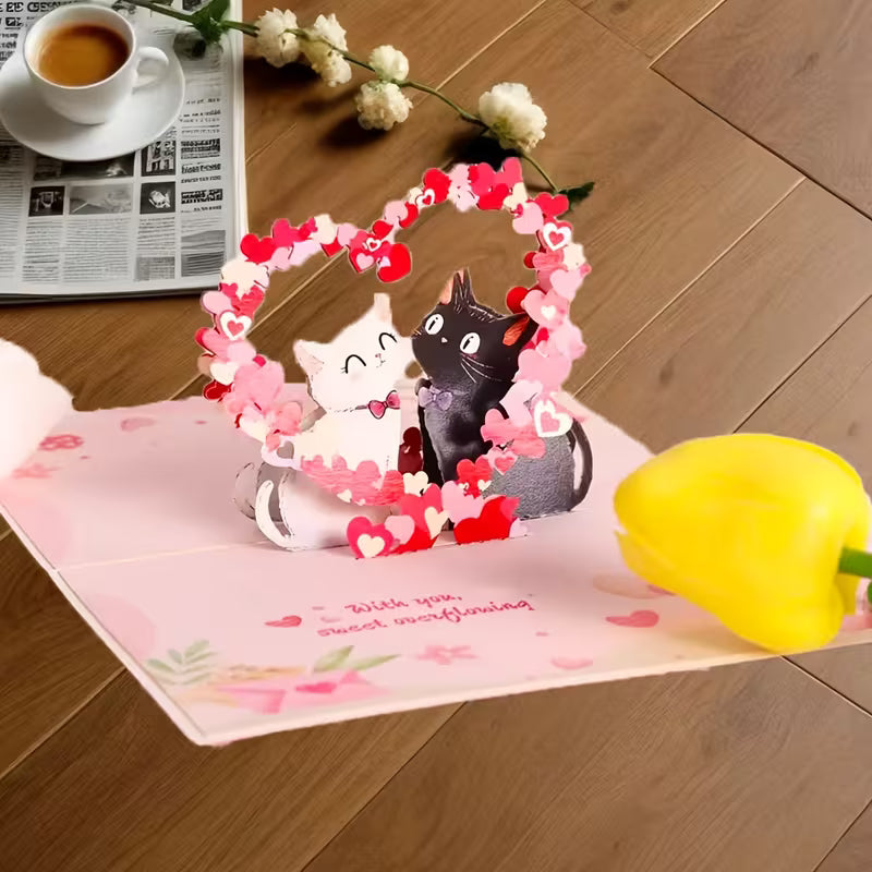 Avattu vaaleanpunainen 3D pop-up -kortti, jossa musta ja valkoinen kissa istuvat sydänkaaren alla ja teksti 'With you, sweet overflowing