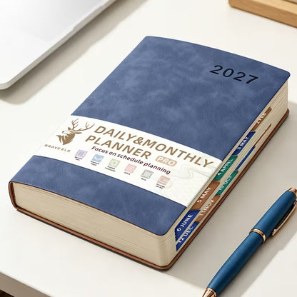 Tuotekuva lilasta A5-kokoisesta Daily & Monthly Planner Pro 2027 -kalenterista, jossa on pehmeä tekonahkakansi, värikkäät kuukausi-indeksit ja lila kirjoituskynä.   