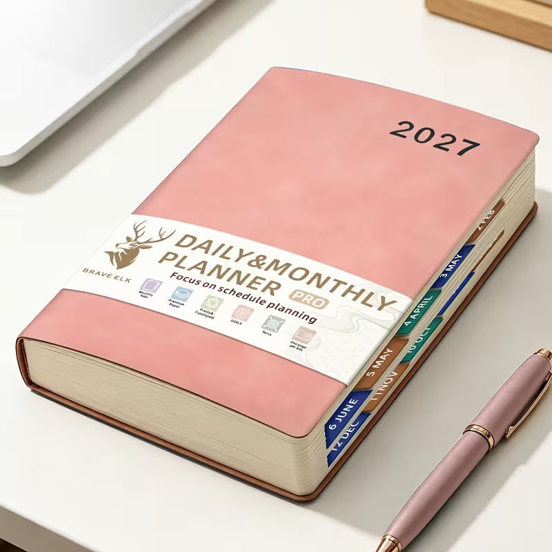 Tuotekuva lilasta A5-kokoisesta Daily & Monthly Planner Pro 2027 -kalenterista, jossa on pehmeä tekonahkakansi, värikkäät kuukausi-indeksit ja lila kirjoituskynä.   