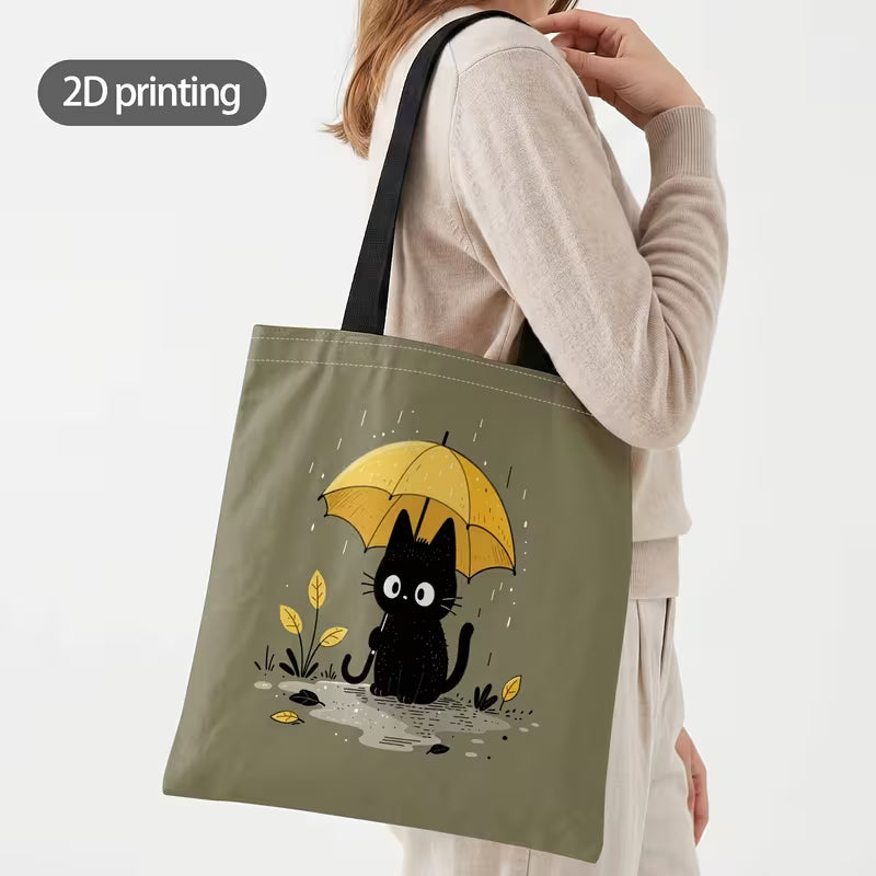 Tuotekuva salvianvihreästä kangaskassista, jossa on 2D-printtikuviointi mustasta kissasta keltaisen sateenvarjon alla sadepäivänä.