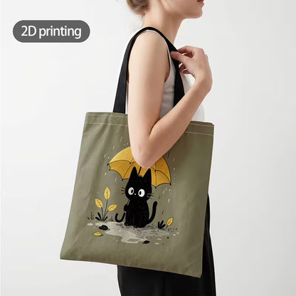 Tuotekuva salvianvihreästä kangaskassista, jossa on 2D-printtikuviointi mustasta kissasta keltaisen sateenvarjon alla sadepäivänä.