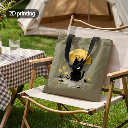 Tuotekuva salvianvihreästä kangaskassista, jossa on 2D-printtikuviointi mustasta kissasta keltaisen sateenvarjon alla sadepäivänä.