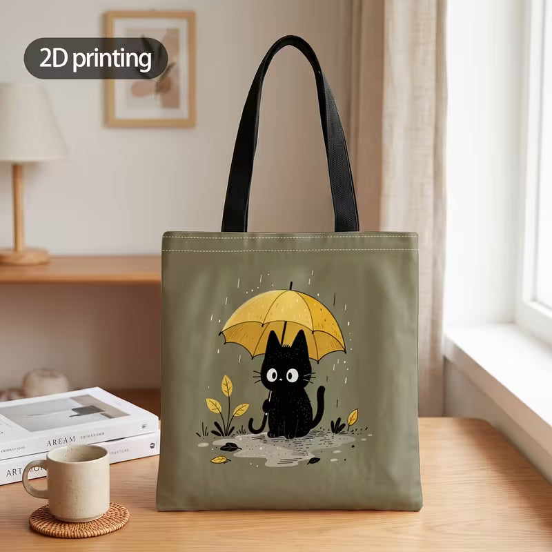 Tuotekuva salvianvihreästä kangaskassista, jossa on 2D-printtikuviointi mustasta kissasta keltaisen sateenvarjon alla sadepäivänä.