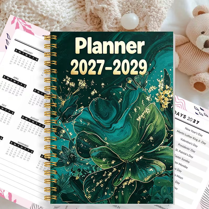 Tuotekuva Planner 2027-2029 -kalenterista, jossa on tummanvihreä fluid art -tyylinen kukkakansi kultahippusilla ja kultainen kierresidonta.   