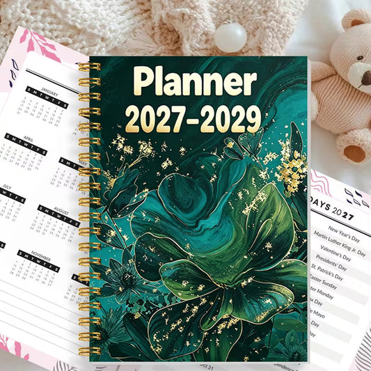 Tuotekuva Planner 2027-2029 -kalenterista, jossa on tummanvihreä fluid art -tyylinen kukkakansi kultahippusilla ja kultainen kierresidonta.   