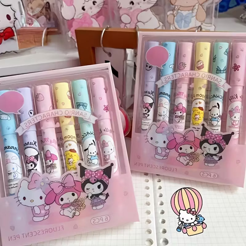 Kuusi pastellinväristä korostuskynää, joissa on Hello Kitty- ja Sanrio-hahmojen kuvia. Kynät on aseteltu avatun muistikirjan viereen valkoisella pöydällä