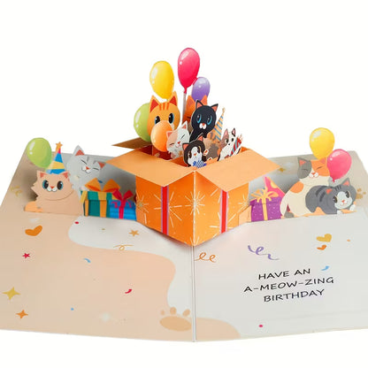 Avattu 3D pop-up -syntymäpäiväkortti, jossa oranssista lahjalaatikosta kurkistaa useita erivärisiä kissoja ja ilmapalloja sekä teksti Have an A-meow-zing birthday.