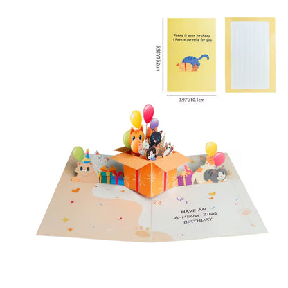 Avattu 3D pop-up -syntymäpäiväkortti, jossa oranssista lahjalaatikosta kurkistaa useita erivärisiä kissoja ja ilmapalloja sekä teksti Have an A-meow-zing birthday.