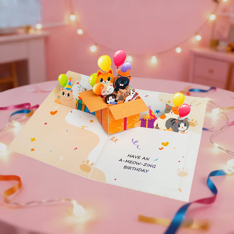 Avattu 3D pop-up -syntymäpäiväkortti, jossa oranssista lahjalaatikosta kurkistaa useita erivärisiä kissoja ja ilmapalloja sekä teksti Have an A-meow-zing birthday.