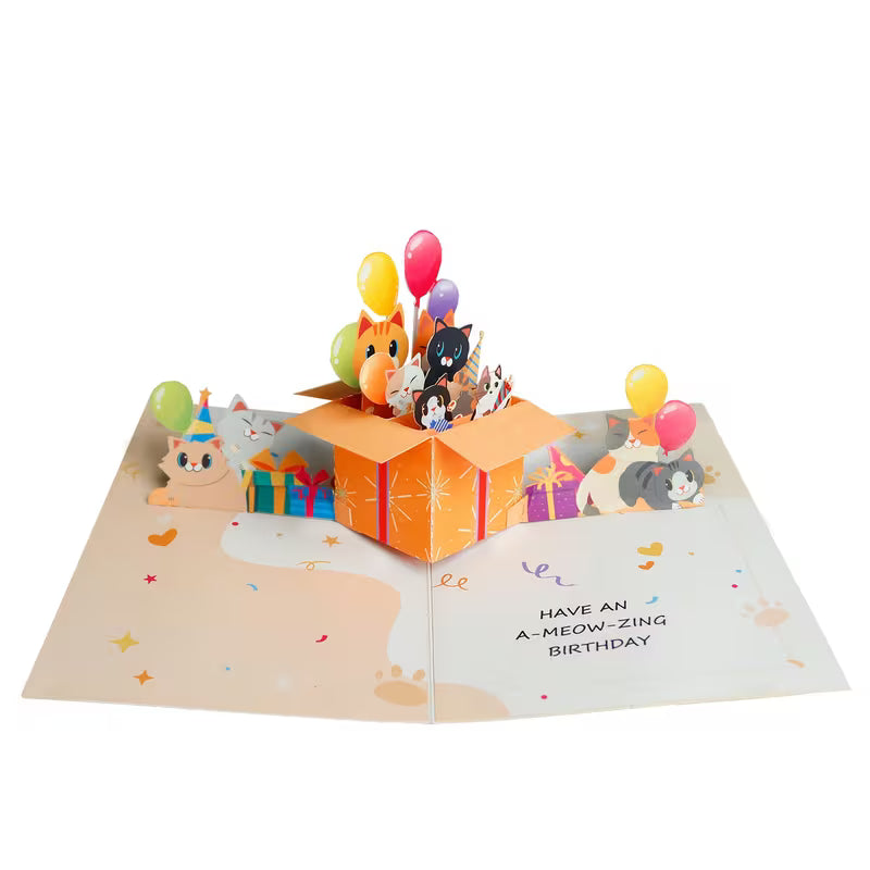Avattu 3D pop-up -syntymäpäiväkortti, jossa oranssista lahjalaatikosta kurkistaa useita erivärisiä kissoja ja ilmapalloja sekä teksti Have an A-meow-zing birthday.