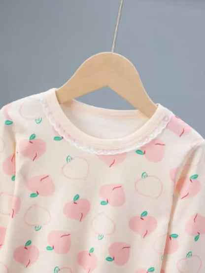 Vaaleanpunaisella persikkakuviolla koristeltu lasten puuvillapyjama, jossa on siro pitsireunus pääntiessä.