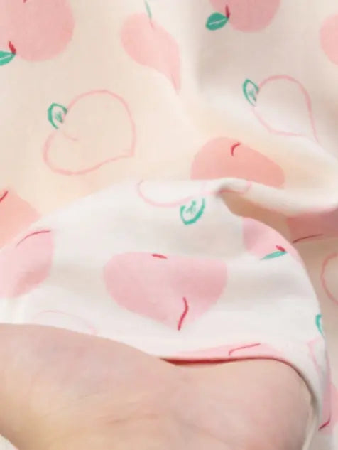 Vaaleanpunaisella persikkakuviolla koristeltu lasten puuvillapyjama, jossa on siro pitsireunus pääntiessä.