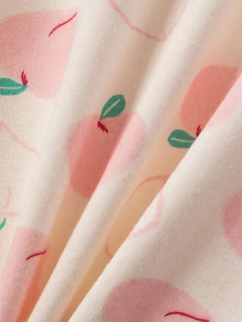Vaaleanpunaisella persikkakuviolla koristeltu lasten puuvillapyjama, jossa on siro pitsireunus pääntiessä.
