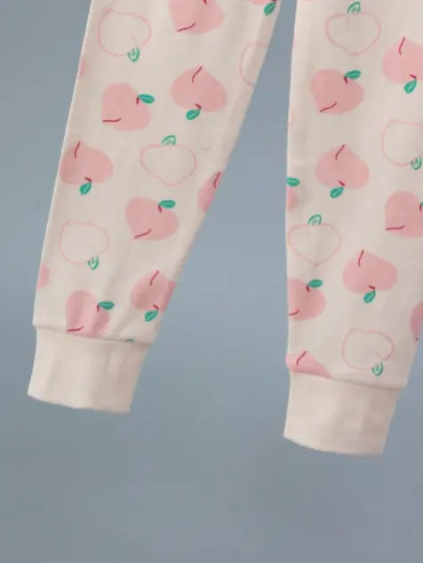 Vaaleanpunaisella persikkakuviolla koristeltu lasten puuvillapyjama, jossa on siro pitsireunus pääntiessä.