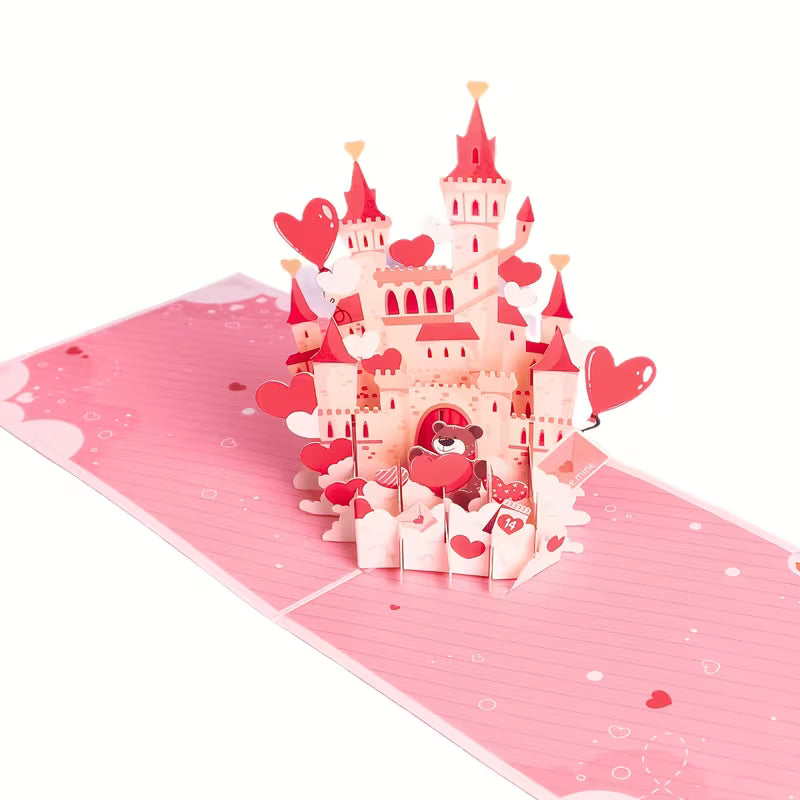 Avattu 3D pop-up -kortti, josta nousee näyttävä vaaleanpunainen linna täynnä sydämiä ja suloinen nallekarhu, kuvattuna vaaleanpunaisella alustalla.