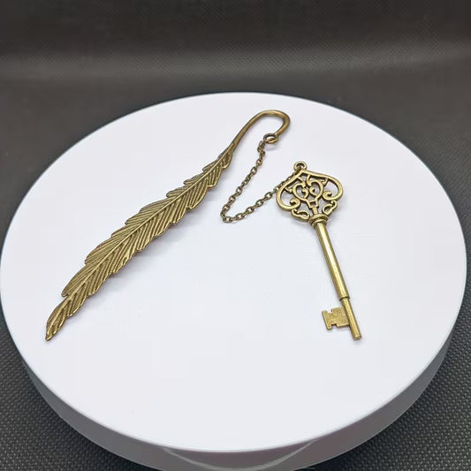 Elegantti metallinen höyhenen muotoinen kirjanmerkki, jossa on hienostuneita kaiverruksia, lepäämässä vanhan nahkakantisen kirjan sivujen päällä.