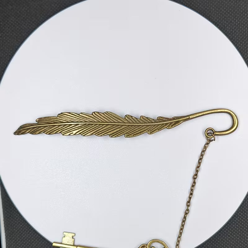 Elegantti metallinen höyhenen muotoinen kirjanmerkki, jossa on hienostuneita kaiverruksia, lepäämässä vanhan nahkakantisen kirjan sivujen päällä.