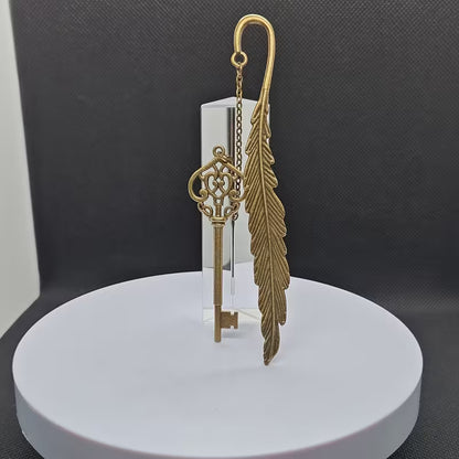 Elegantti metallinen höyhenen muotoinen kirjanmerkki, jossa on hienostuneita kaiverruksia, lepäämässä vanhan nahkakantisen kirjan sivujen päällä.